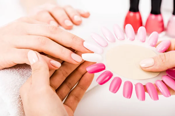 Partial view of manicurist holding nail polish palette while woman choose color — Stock Photo