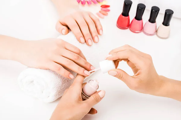 Girl holding hands on towel while manicurist applying nail polish — Stock Photo