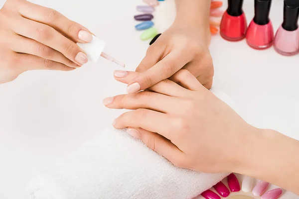 Vista recortada de la manicura sosteniendo el dedo mientras se aplica esmalte de uñas - foto de stock