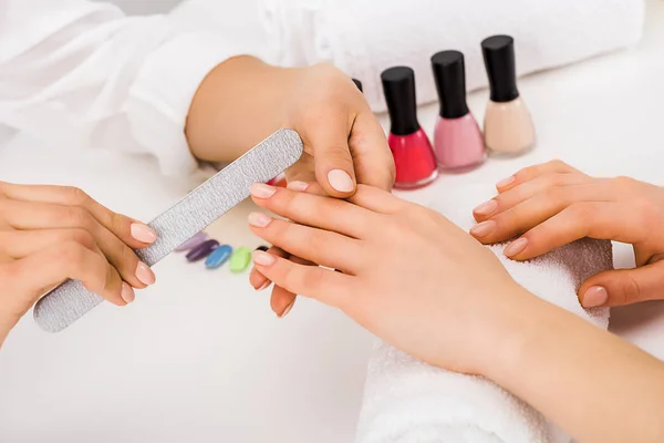 Vista ritagliata della donna che tiene la mano sull'asciugamano mentre la manicurista fa la forma delle unghie — Foto stock