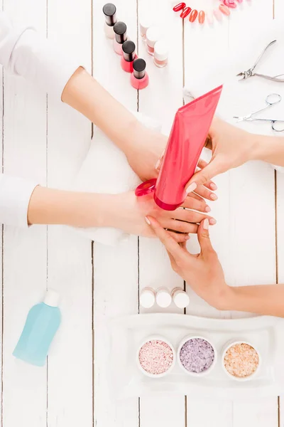 Vista dall'alto della manicure usando la crema per le mani sulla superficie di legno — Foto stock