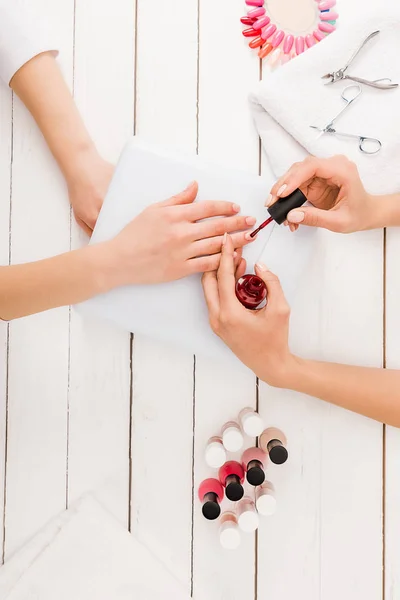 Vue du dessus de manucure appliquant vernis à ongles rouge — Photo de stock