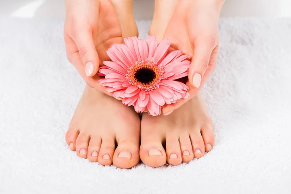 Partial view of barefoot woman standing on towel and holding flower — Stock Photo