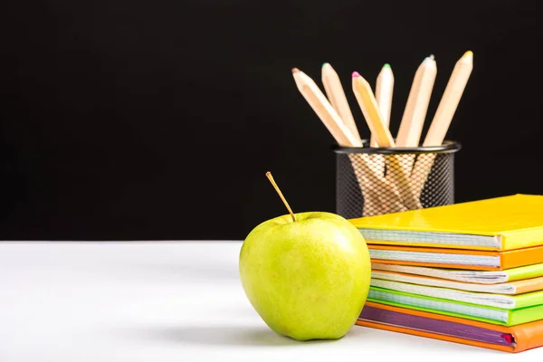 Барвисті блокноти, олівці та яблуко ізольовані на чорному з копіювальним простором — стокове фото