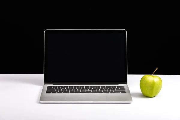 Manzana y portátil con pantalla en blanco en el escritorio aislado en negro - foto de stock