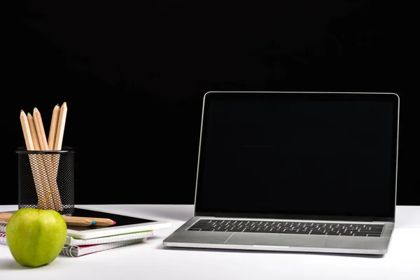 Pomme, cahiers, crayons et ordinateur portable avec écran blanc isolé sur noir — Photo de stock