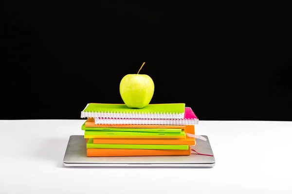 Carnets colorés, pomme et ordinateur portable sur le bureau isolé sur noir — Photo de stock
