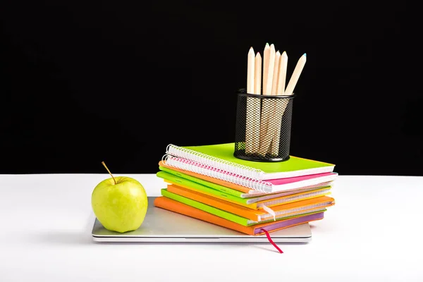 Carnets colorés, pomme et ordinateur portable sur le bureau isolé sur noir — Photo de stock