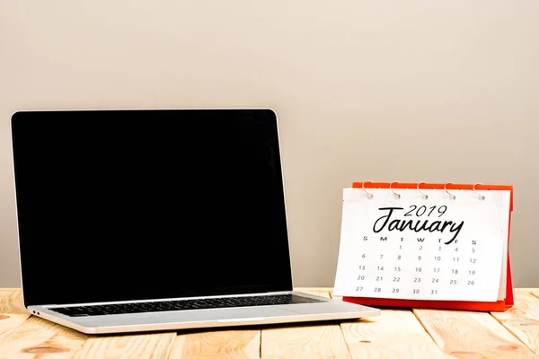 Calendar with 'january 2019' lettering and laptop with blank screen isolated on beige — Stock Photo