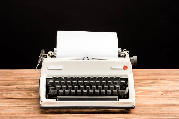 Винтажная пишущая машинка с бумагой на деревянном столе, изолированная на черном — стоковое фото