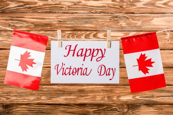 Top view of canadian flags and card with 'happy victoria day' lettering on wooden background — Stock Photo