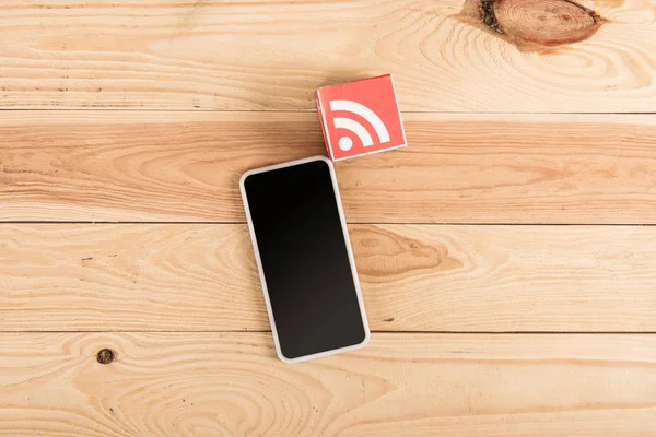Vista superior del icono de alimentación RSS y el teléfono inteligente con pantalla en blanco en la mesa de madera - foto de stock