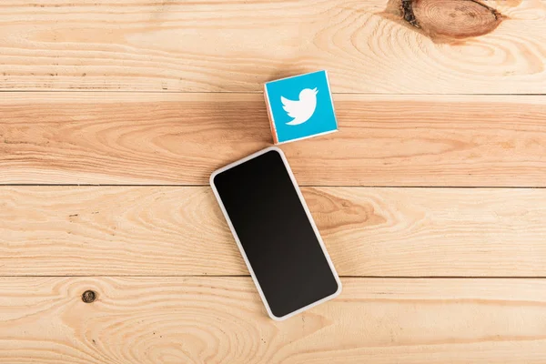 Вид сверху на значок твиттера и смартфон с пустым экраном на деревянном столе — стоковое фото