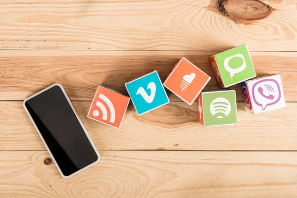 Top view of smartphone with blank screen and website icons on wooden background — Stock Photo
