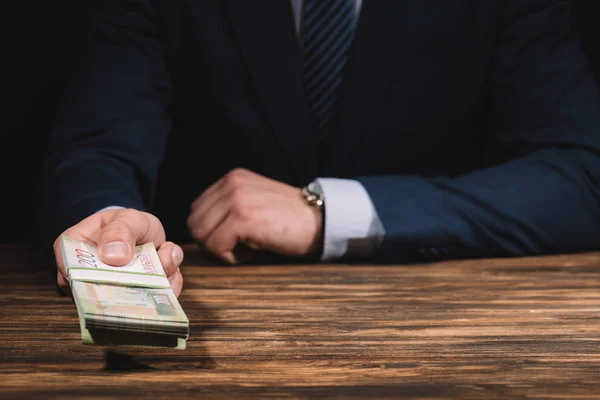 Обрезанный снимок бизнесмена в костюме с российскими рублями банкнотами в руке над деревянным столом — стоковое фото
