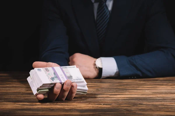 Partial view of businessman holding russian rubles banknotes at wooden table — Stock Photo