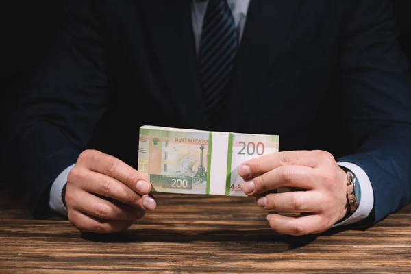 Vista parcial del hombre de negocios en ropa formal con billetes de rublos rusos por encima de la mesa de madera - foto de stock