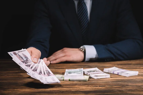 Mid section of businessman in formal wear holding russian rubles banknotes above wooden table — Stock Photo