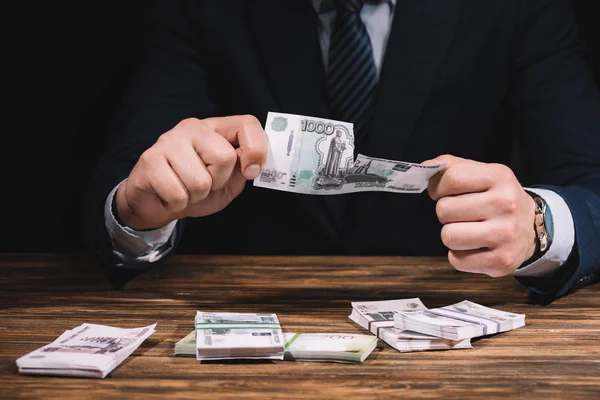 Средняя секция бизнесмена, разрывающего банкноту над деревянным столом русскими рублями — стоковое фото
