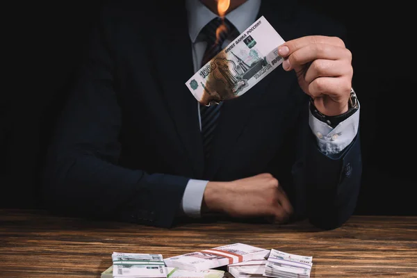 Cropped shot of businessman burning banknote above wooden table with russian rubles — Stock Photo