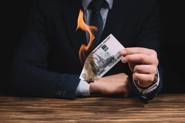 Sección media de empresario quema de billetes de rublos rusos por encima de la mesa de madera - foto de stock