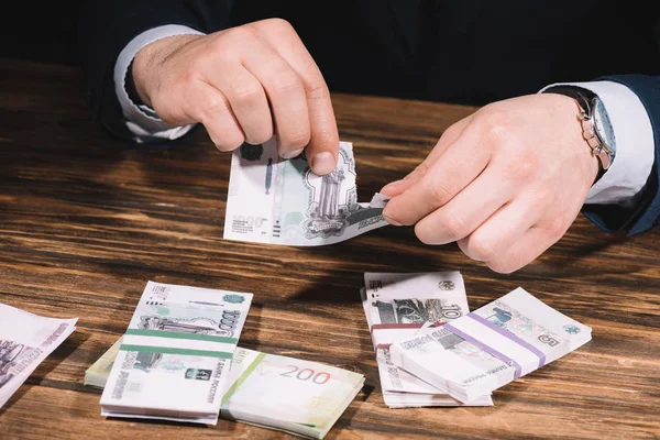 Recortado tiro de hombre de negocios rasgando billete por encima de la mesa de madera con rublos rusos - foto de stock