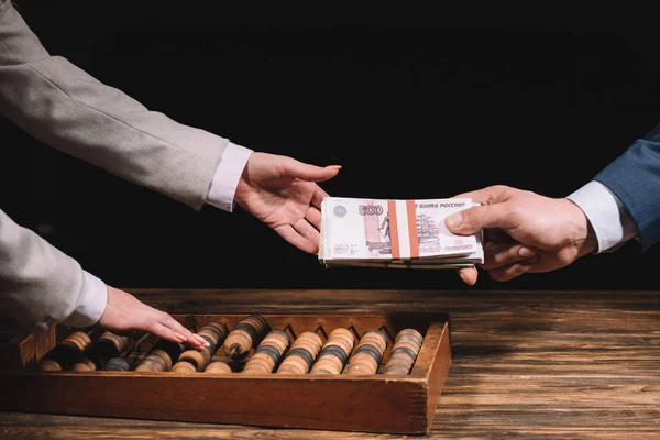 Tiro cortado de empresário dando rublos russos para empresária usando ábaco na mesa de madeira — Fotografia de Stock