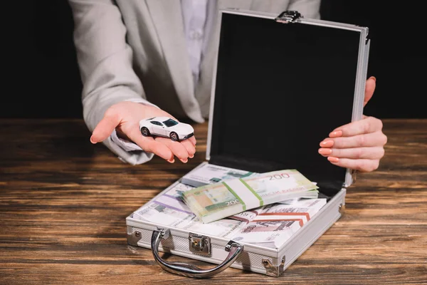 Cropped shot of businesswoman holding model car and suitcase safe box with russian rubles on wooden table — Stock Photo