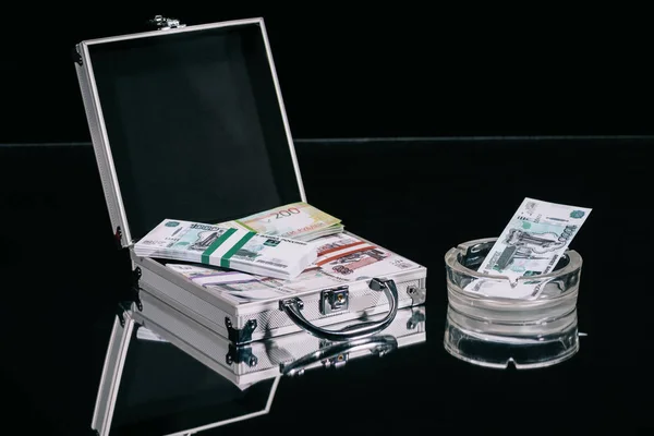 Russische Rubel-Banknoten im Koffersafe und Geld im Aschenbecher auf schwarz — Stockfoto