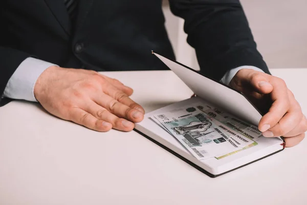 Partial view of businessman holding notebook with russian rubles banknotes at workplace — Stock Photo