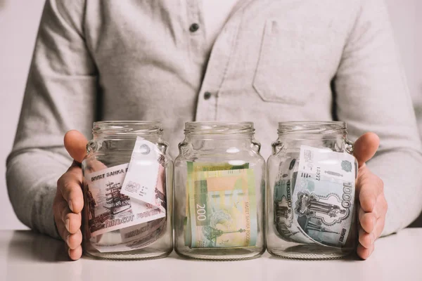 Cropped shot of man holding glass jars with russian rubles banknotes — Stock Photo