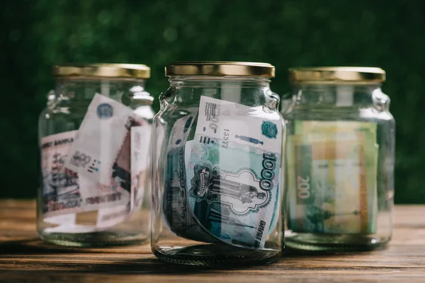 Vista de cerca de frascos de vidrio con billetes de rublos rusos en la mesa de madera - foto de stock