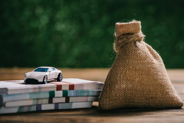 Close-up view of sackcloth bag with money, rubles banknotes and model car on wooden table — Stock Photo