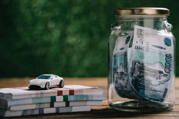Close-up view of glass jar with money, rubles banknotes and model car on wooden table — Stock Photo