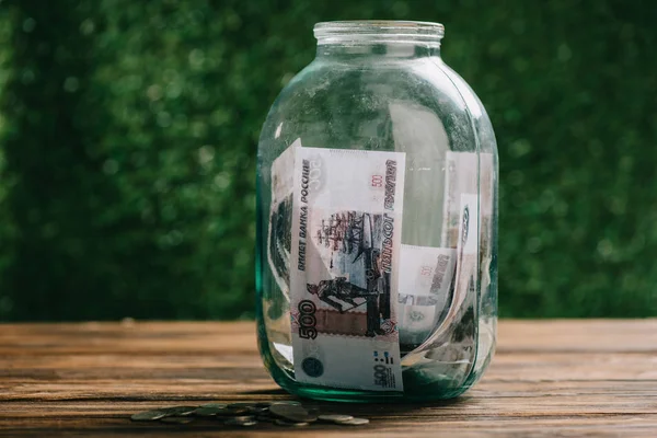 Vista de cerca del frasco de vidrio con billetes de rublos y monedas en la mesa de madera - foto de stock