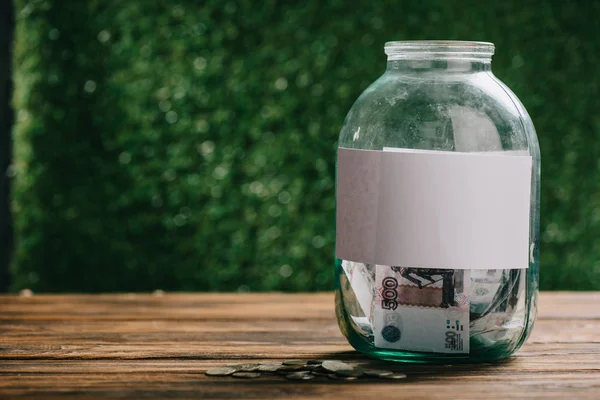 Tarro de vidrio con etiqueta en blanco y rublos rusos en la mesa de madera — Stock Photo