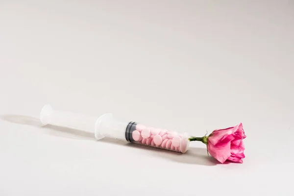 Studio shot of pink flower, syringe and pills on grey — Stock Photo