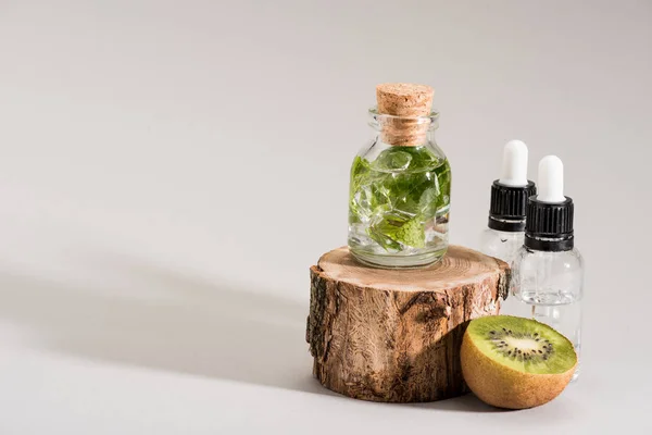 Photo studio de bouteille en verre avec des bouteilles de menthe, kiwi et sérum sur gris — Photo de stock