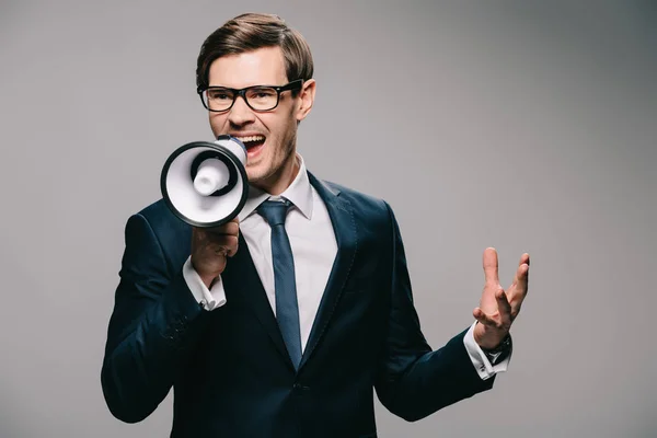 Empresário irritado em terno gritando em megafone no fundo cinza — Fotografia de Stock