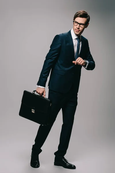 Serious businessman standing in suit with briefcase on grey background — Stock Photo