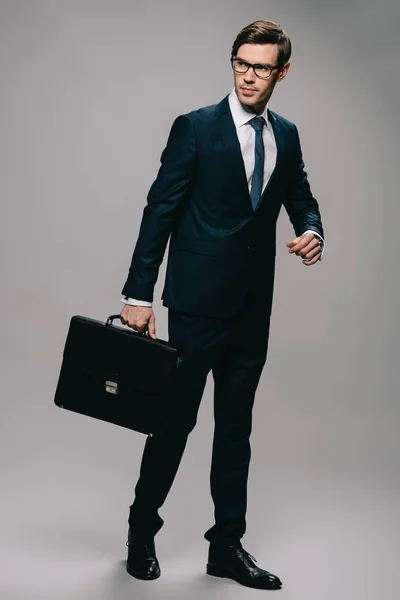 Serious businessman in suit holding briefcase on grey background — Stock Photo