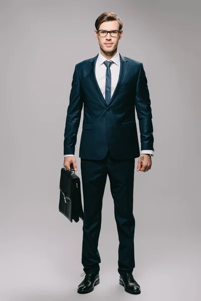 Confident businessman in suit holding briefcase on grey background — Stock Photo