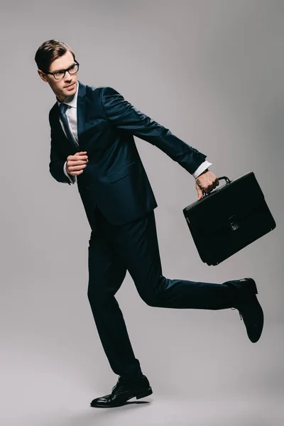 Confident businessman in suit running with briefcase on grey background — Stock Photo
