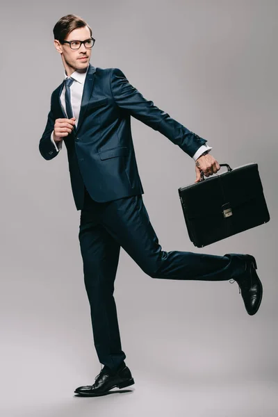 Handsome businessman in suit running with briefcase on grey background — Stock Photo