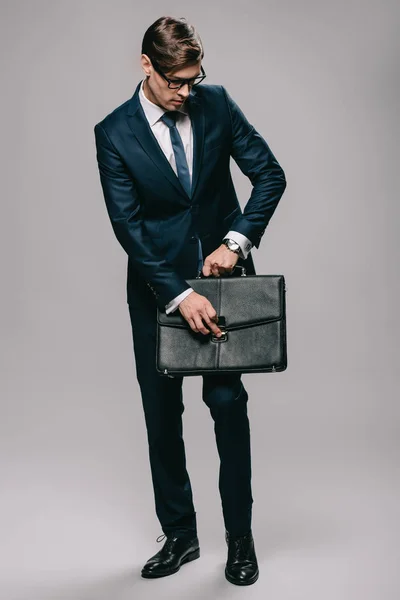 Красивый бизнесмен в очках открывает портфель на сером фоне — Stock Photo