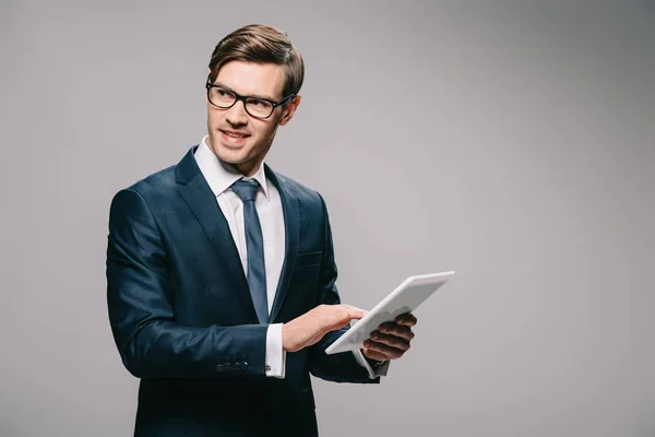 Веселий бізнесмен в окулярах, використовуючи цифровий планшетний ізольовані на сірому — стокове фото