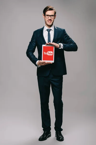 Handsome businessman holding digital tablet with youtube app on screen on grey background — Stock Photo