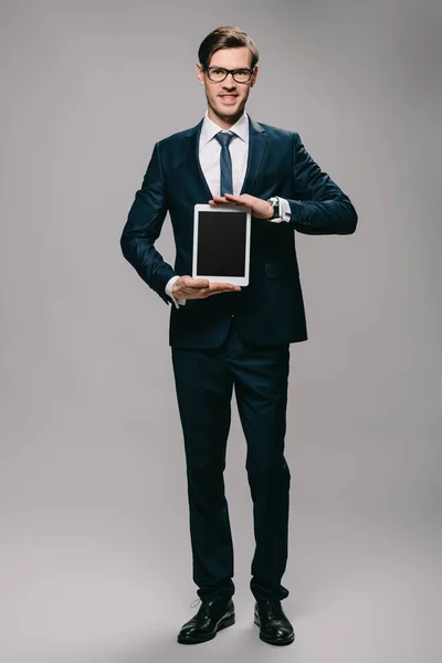 Cheerful businessman holding digital tablet with blank screen on grey background — Stock Photo