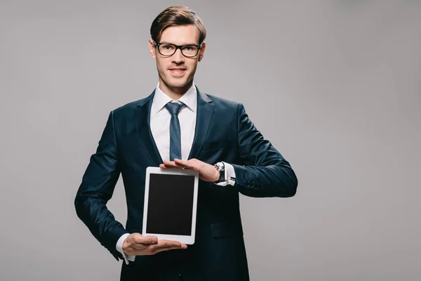 Alegre hombre de negocios sosteniendo tableta digital con pantalla en blanco aislado en gris - foto de stock