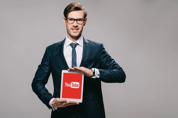 Cheerful businessman holding digital tablet with youtube app on screen isolated on grey — Stock Photo